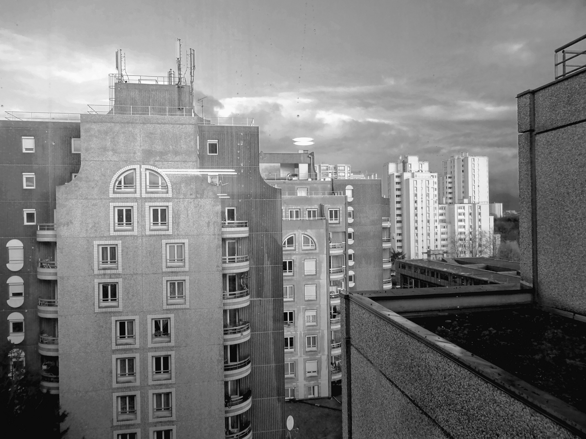 Vue d'une fenêtre du Conseil Général, la pluie et les reflets sur la vitre. Perspective d'immeubles.